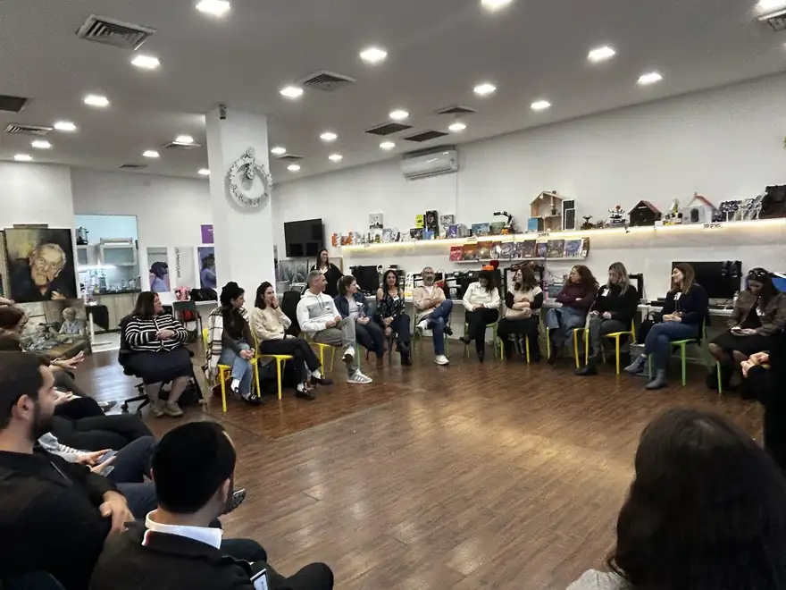קבוצת מבוגרים יושבת במעגל בחלל המתחם, ואישה עומדת ומדברת