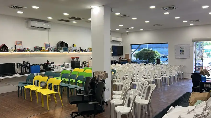 חלל המתחם: עמדות מחשב, כיסאות צבעוניים, מדפי ציוד ושורות כיסאות לבנים