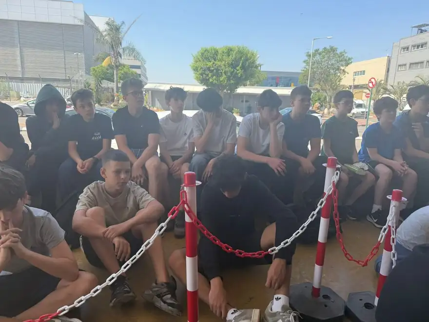 קבוצת תלמידים יושבת בחוץ ומקשיבה להסבר