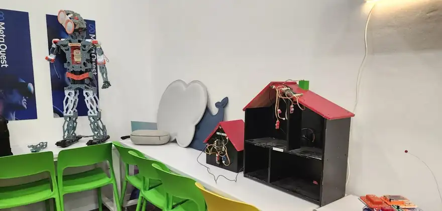 רובוט דמוי אדם עומד בפינת המתחם ליד כיסאות ירוקים