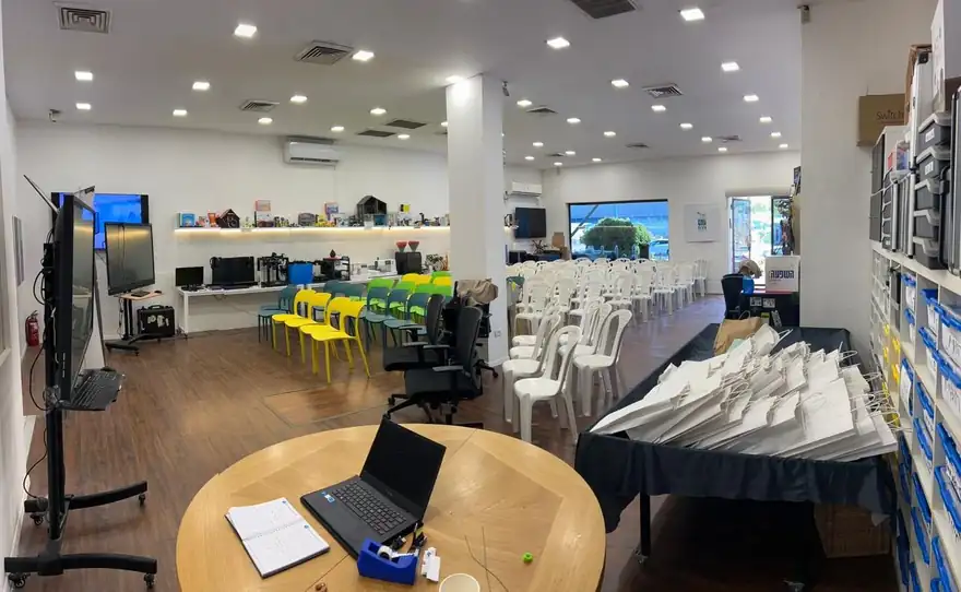 חלל הלמידה במתחם: שולחנות עבודה עם כיסאות צבעוניים ומסכים על הקירות