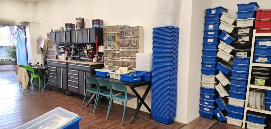 חלל עבודה עם שולחנות ומדפים מלאים בקופסאות ציוד צבעוניות